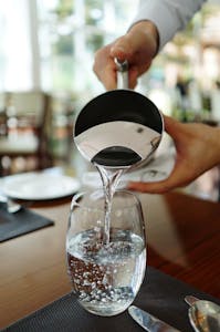 Close-up of water being poured into a glass in a restaurant setting.