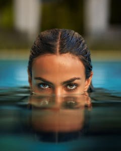 Close-up shot of a woman's eyes above water, conveying mystery and allure in a swimming pool setting.