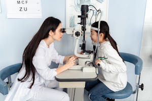 Optometrist performing vision test on child using medical equipment indoors.